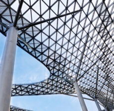Modern lattice roof structure supported by tall columns against a blue sky.