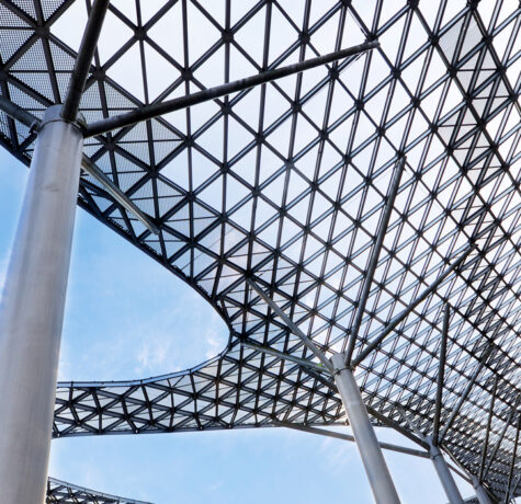 Modern lattice roof structure supported by tall columns against a blue sky.