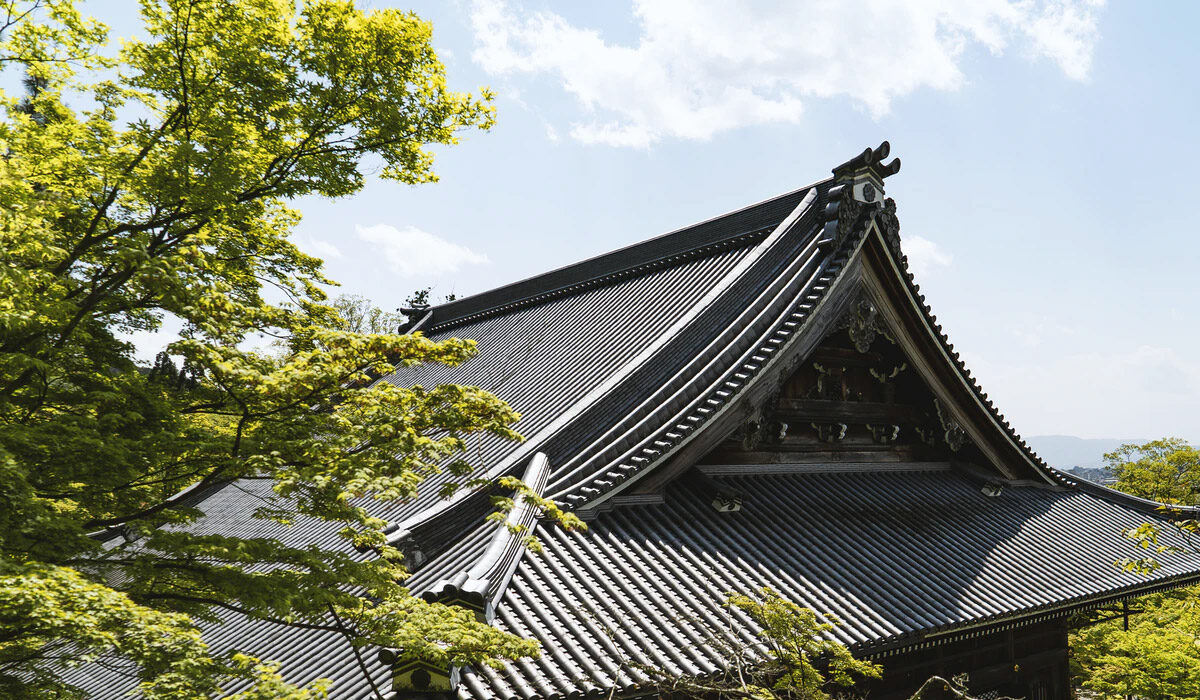 Traditional Japanese temple roof with intricate details and green foliage nearby.