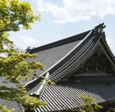 Traditional Japanese temple roof with intricate details and green foliage nearby.
