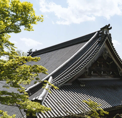 Traditional Japanese temple roof with intricate details and green foliage nearby.