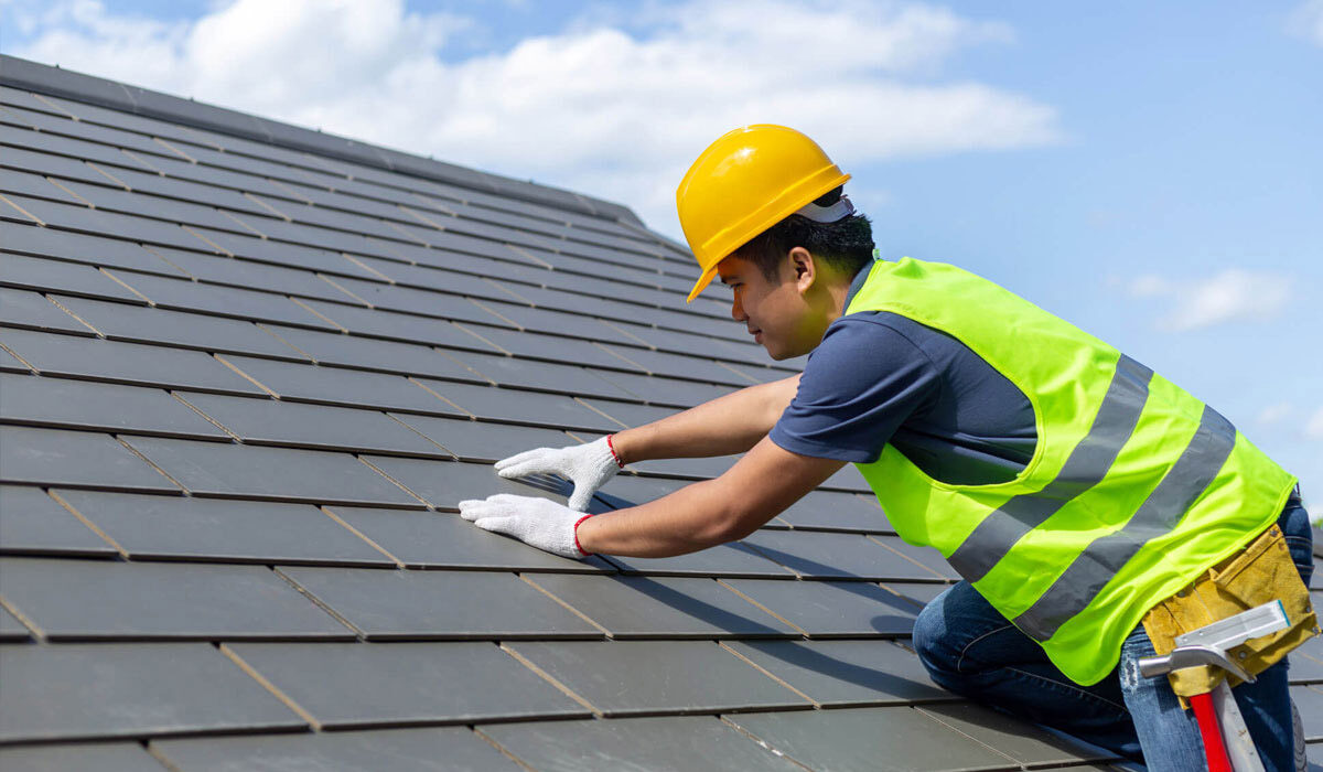 Construction worker installing roof tiles while wearing safety gear.
