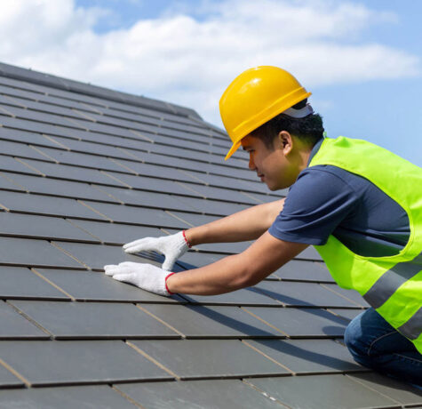 Construction worker installing roof tiles while wearing safety gear.