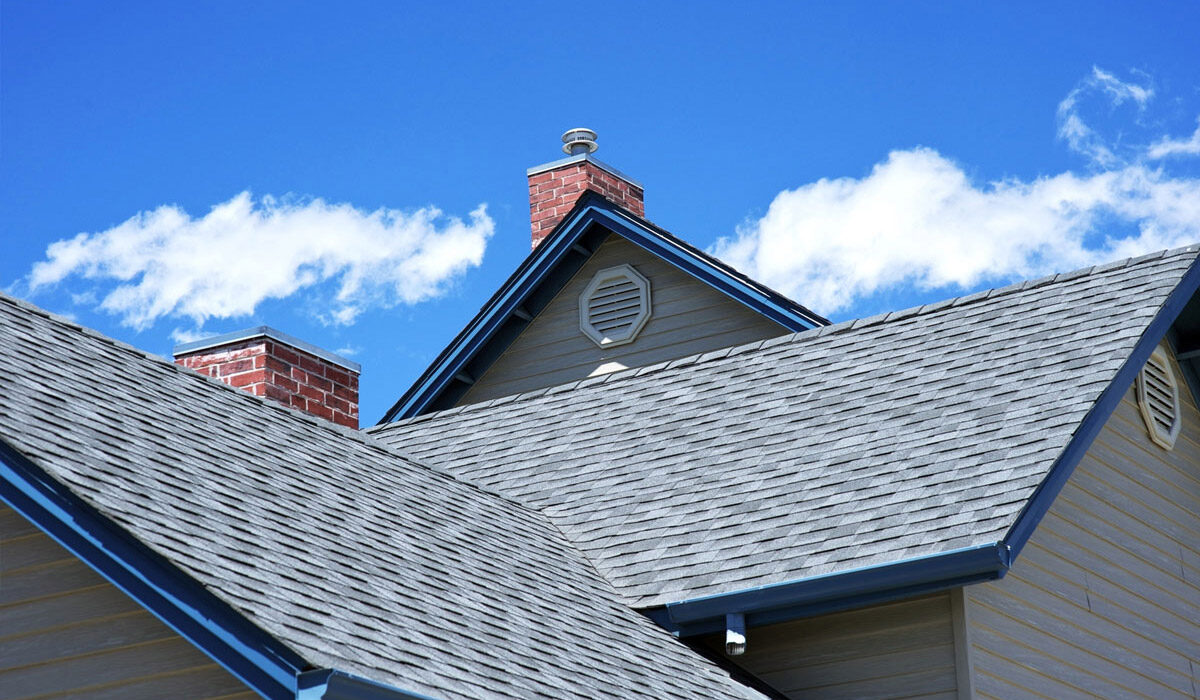 Close-up of rooftops with gray shingles under a blue sky with clouds.