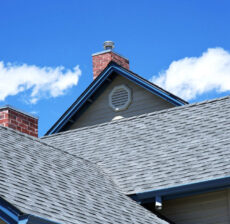 Close-up of rooftops with gray shingles under a blue sky with clouds.