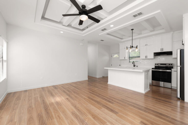 Modern kitchen and living area with wooden floors and ceiling fan.