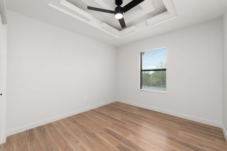 Empty room with wooden floor, ceiling fan, and window.