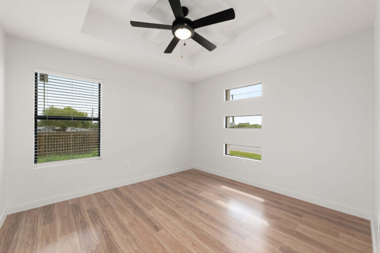 Bright empty room with wood floors and ceiling fan.