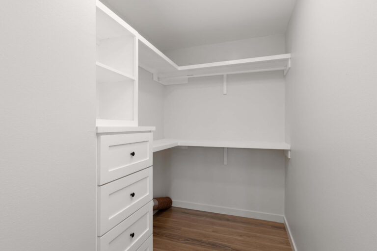 Empty walk-in closet with white shelves and drawers.