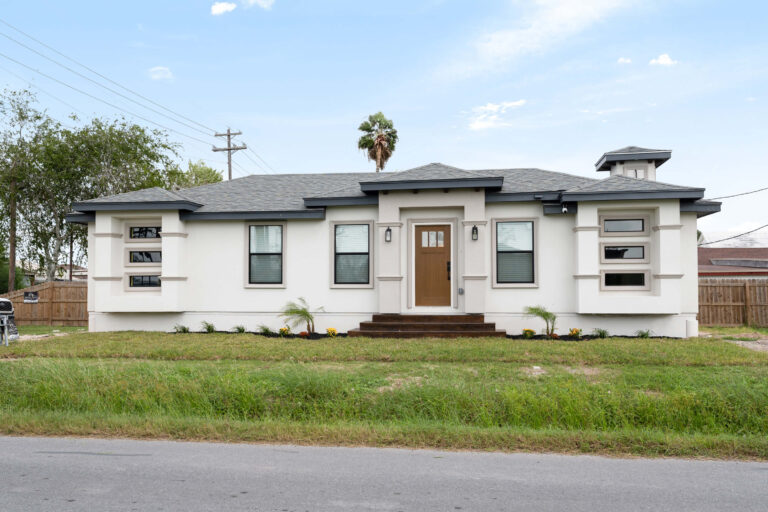 White single-story house with dark roof and wooden front door.